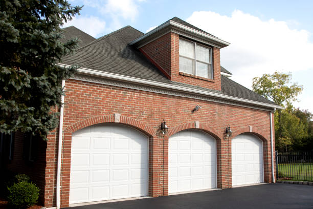 A brick 3-car garage has three white doors and a room with a window sitting above it.